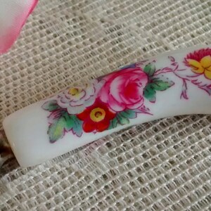 May include: A white ceramic butter knife with a floral design. The handle features pink, red, white, and yellow flowers with green leaves.