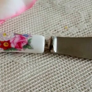 May include: A white ceramic butter knife with a floral design and a silver blade. The handle features pink, red, and blue flowers.