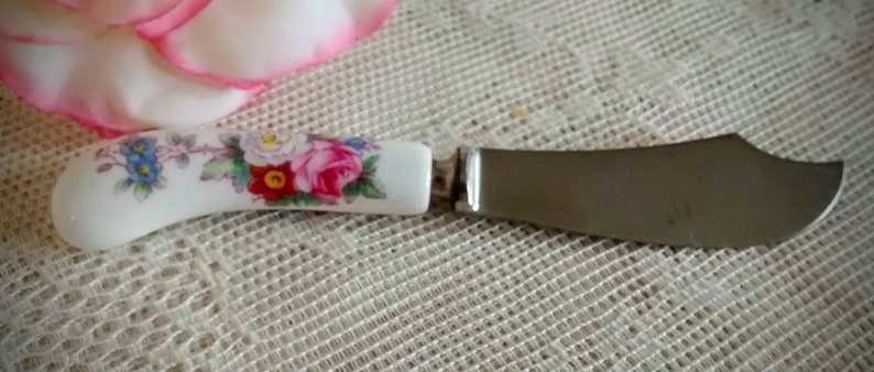 May include: A white ceramic butter knife with a floral design and a silver blade. The handle features pink, red, and blue flowers.