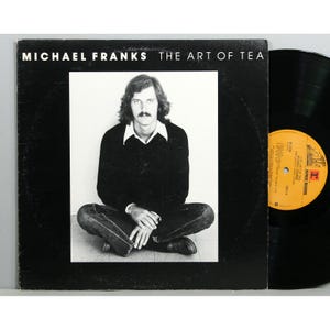 May include: A black vinyl record album by Michael Franks, titled "The Art of Tea." The album cover features a black and white photo of a man with long hair and a mustache. The album is a vintage music item.