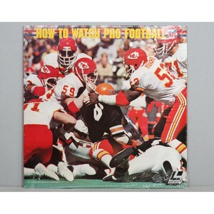 May include: A vintage record album cover featuring a football game in progress. The cover is red, white, and blue with the text "HOW TO WATCH PRO FOOTBALL" and the NFL logo. The image shows a group of football players in red and white uniforms, with one player in a black uniform being tackled.