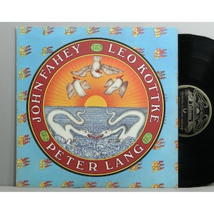 May include: A vintage vinyl record album featuring the artists John Fahey, Leo Kottke, and Peter Lang. The album cover has a blue background with a circular design of birds, water, and a sunset. The record is black.