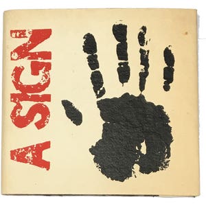 Pode incluir: Uma capa de livro vintage com o título "A SIGN" em letras vermelhas. Uma impressão de mão preta está centralizada na capa.