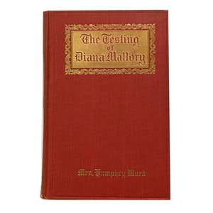 Pode incluir: Um livro vermelho com letras douradas na capa. O título é "The Testing of Diana Mallory" de Mrs. Humphry Ward.