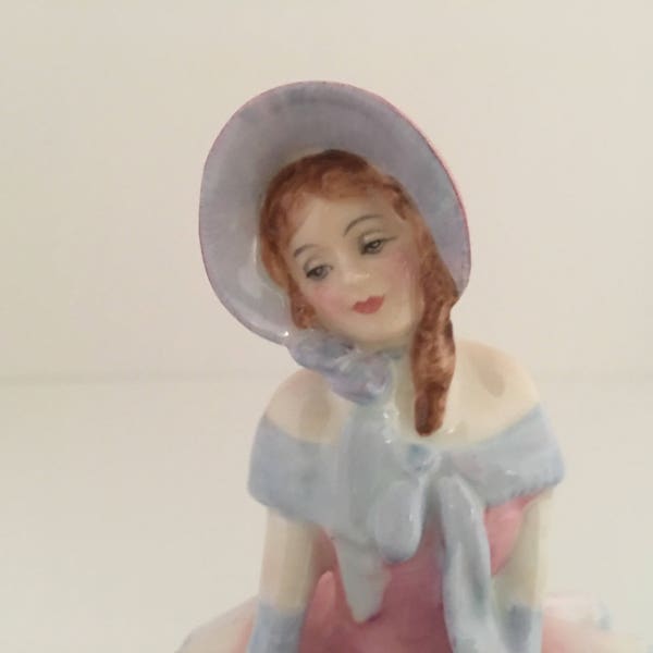 Figurine de Royal Doulton presque antique. 1935 le 1er édition RÊVERIES. Etat neuf. Fille assise avec bonnet et des fleurs.