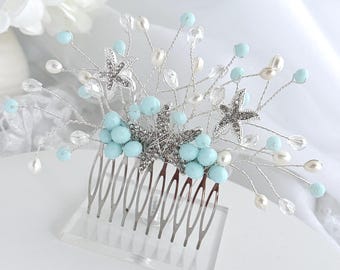 May include: A silver-toned hair comb featuring three starfish accents, light blue spherical beads, and clear crystal-like beads on flexible wire branches. The decorative elements are arranged in a fan-like spray extending from the metal comb base.