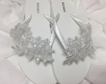 May include: Pair of white flip flops with silver floral embellishments. The flip flops are labeled "Old Navy".