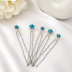 May include: A set of five silver-toned metal hair pins, each featuring a small, faceted, bright blue star-shaped crystal at the top. The pins have a U-shaped design with wavy prongs and are connected to the crystal by a thin, coiled wire detail.