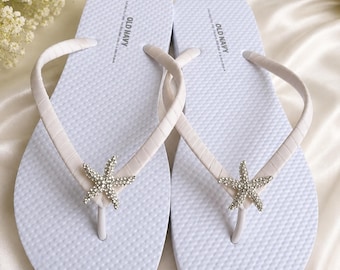 Chanclas color marfil con estrellas de mar de diamantes de imitación para una ceremonia en la playa. Chanclas color marfil con temática náutica para una boda en la costa.