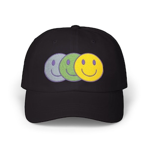 May include: Black baseball cap featuring three embroidered smiley faces in gray, green, and yellow. The smiley faces are arranged horizontally, with the yellow one overlapping the green one. The cap has a curved brim and a structured crown.