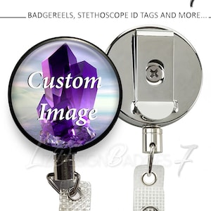 May include: A silver retractable badge reel with a clear round plastic cover featuring a purple crystal image and the text "Custom Image". The reel has a heavy duty steel cable and a white clip.