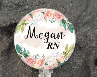 May include: A white round badge holder with a floral design and the name Megan RN printed on it. The badge holder is attached to a clear plastic retractable badge reel.