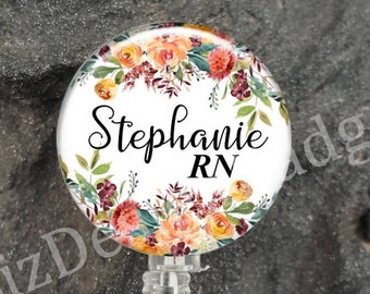 May include: A white badge reel with a round, floral-patterned badge holder. The badge holder has the name "Stephanie RN" printed in black cursive font.