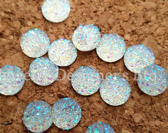 Op de afbeelding: Een verzameling van regenboogkleurige, ronde, platte cabochons. De cabochons zijn ongeveer 1,25 cm in diameter en hebben een glinsterende, glitterende afwerking.