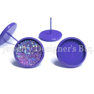 May include: Three purple metal earring settings, two with a post and one with a flat back. One setting is filled with iridescent glitter.