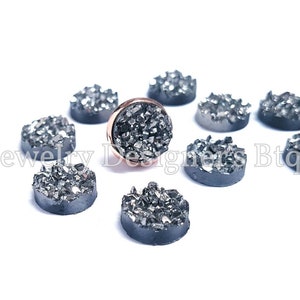 May include: A collection of ten round, black, sparkly, agate cabochons. The cabochons are arranged in a circle around a single, larger cabochon with a rose gold setting.