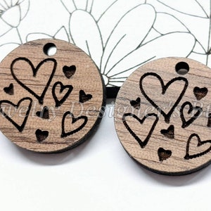 May include: Two round wooden ornaments with a brown wood grain finish. Each ornament has a hole at the top for hanging. The ornaments are decorated with black outlined hearts of various sizes.