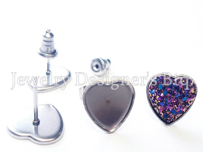May include: A pair of heart-shaped stud earrings with a silver post and back. One earring has a purple and gold glitter heart, and the other earring has a silver heart.