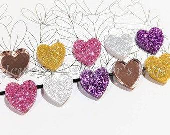 May include: Assortment of ten heart-shaped resin embellishments with glitter. The hearts are in various colors, including gold, silver, pink, purple, and copper.