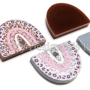 May include: Three half-circle resin shapes with glitter and a rainbow design. The rainbow is pink, white, and gold glitter. The shapes are brown, grey, and silver.