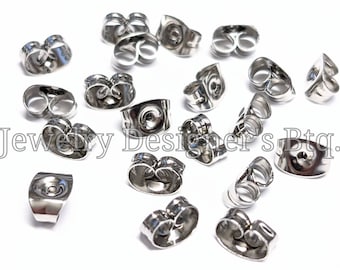 Könnte beinhalten: Nahaufnahme eines Stapels silberner Ohrringverschlüsse. Die Verschlüsse sind aus Metall und haben ein kleines Loch in der Mitte. Sie sind für die Verwendung mit Steckerohrringen konzipiert.