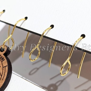 May include: Five gold earring hooks are displayed on a white board with black trim. The hooks are arranged in a row, with the top of each hook facing the viewer. The hooks are all the same size and shape, and they have a smooth, shiny finish.