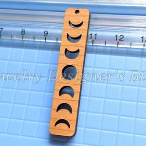May include: A wooden pendant featuring a cutout design of eight moon phases. The pendant is approximately 5 cm tall and is crafted from natural wood.
