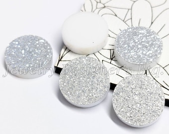May include: Five round, flat, white cabochons. Four of the cabochons are covered in silver glitter. One cabochon is plain white.