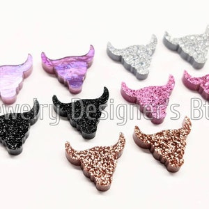 May include: Assortment of ten small, glittery, resin bull skull charms in various colours, including black, silver, pink, and gold.