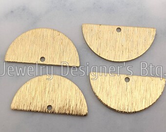 May include: Four gold-colored, half-circle shaped jewelry components with a textured surface and a small hole at the top for stringing. The text "Jewelry Designer's Btq." is visible in the image.