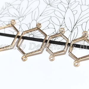 May include: Four gold-toned metal hexagon-shaped jewellery connectors arranged in a row. Each geometric frame features two small circular loops at opposite ends for attachment. The connectors vary slightly in size and have a smooth, metallic finish.