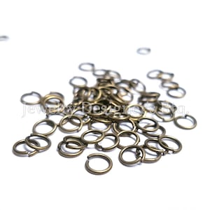 May include: A pile of gold-toned jump rings, a type of jewelry finding used for connecting chains, cords, and other jewelry components.