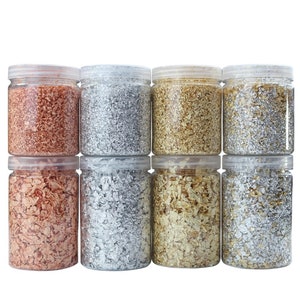 May include: Eight clear plastic jars filled with loose metallic flakes. The jars are arranged in two rows of four. The flakes are in four colors: copper, silver, gold, and a lighter silver.
