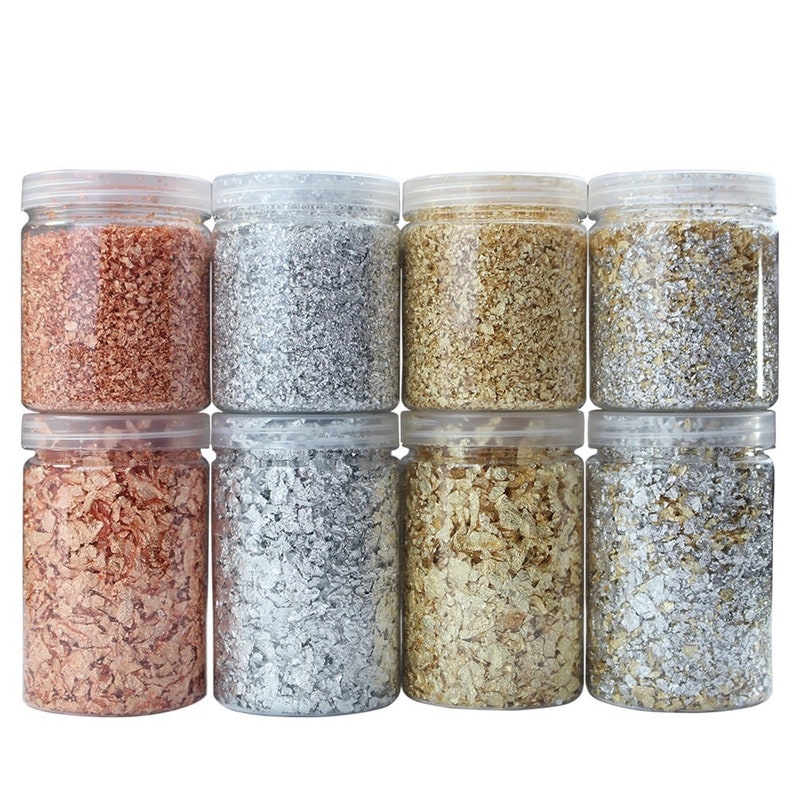 May include: Eight clear plastic jars filled with loose metallic flakes. The jars are arranged in two rows of four. The flakes are in four colors: copper, silver, gold, and a lighter silver.