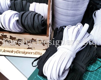 May include: Close-up of white and black elastic cord spools. The spools are arranged in a wooden box with a floral design and the text "@JewelryDesignersBtq".