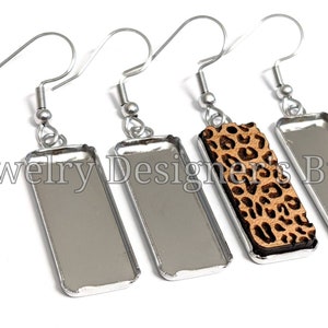 May include: Four silver earring blanks with a leopard print design on one of the blanks. The blanks are rectangular and have a silver hook.