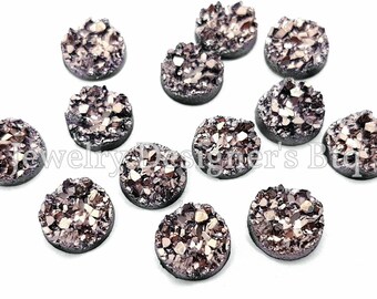 Puede incluir: Una colección de 12 cabujones redondos, de fondo plano, de color plateado metálico y dorado. Los cabujones tienen un diámetro aproximado de 2,5 cm y una textura natural, irregular y cristalina.