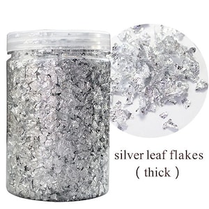 May include: A clear jar filled with silver leaf flakes. The jar has a white lid and the label reads "silver leaf flakes (thick)".