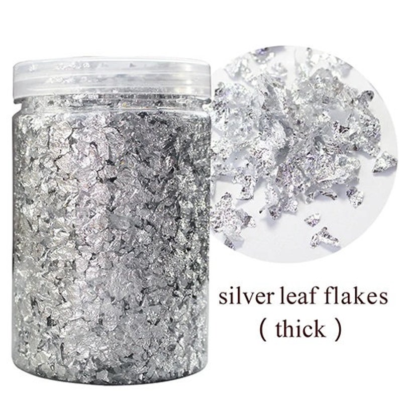 May include: A clear jar filled with silver leaf flakes. The jar has a white lid and the label reads "silver leaf flakes (thick)".