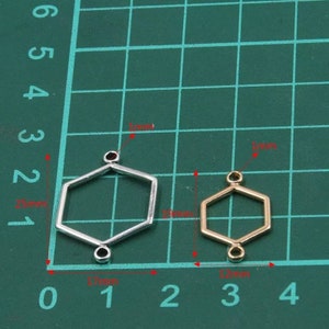 May include: Two hexagonal metal jewellery connectors with small loops at the top and bottom. The larger silver connector measures 25mm by 17mm, while the smaller gold connector measures 19mm by 12mm. Both feature a 1mm thickness for jewellery making.