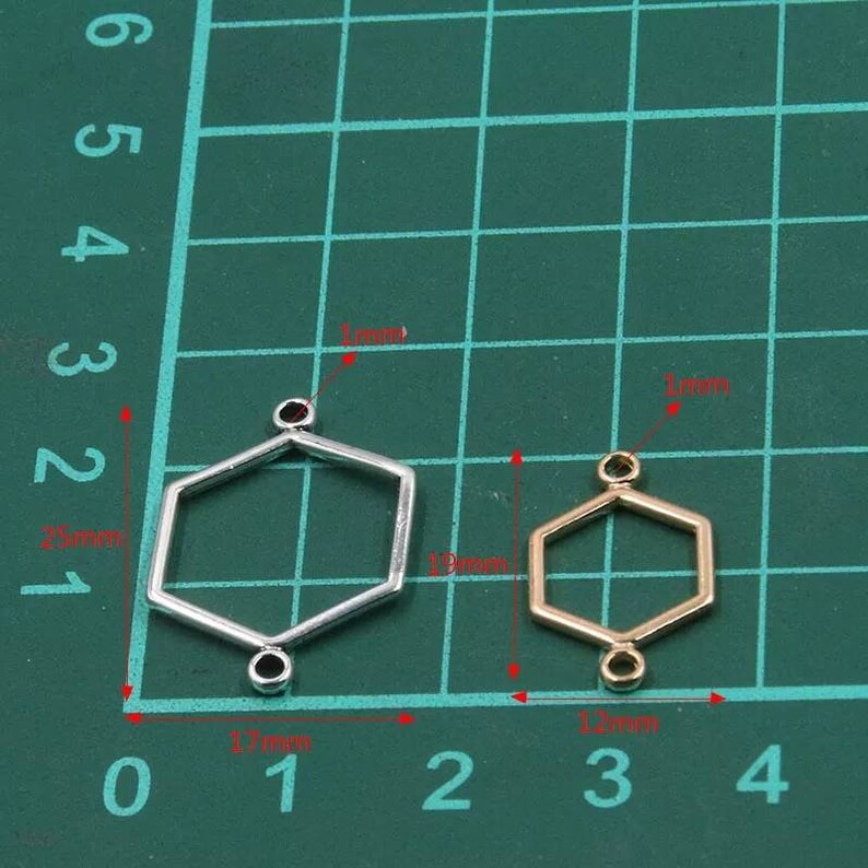 May include: Two hexagonal metal jewellery connectors with small loops at the top and bottom. The larger silver connector measures 25mm by 17mm, while the smaller gold connector measures 19mm by 12mm. Both feature a 1mm thickness for jewellery making.