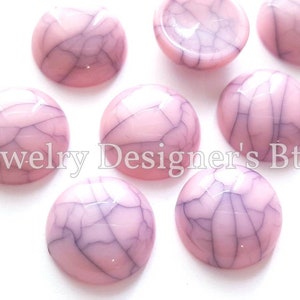 K&ouml;nnte beinhalten: Rosa und wei&szlig;e marmorierte Cabochons mit einer gecrackten Oberfl&auml;che. Die Cabochons sind rund und haben eine glatte, gl&auml;nzende Oberfl&auml;che.