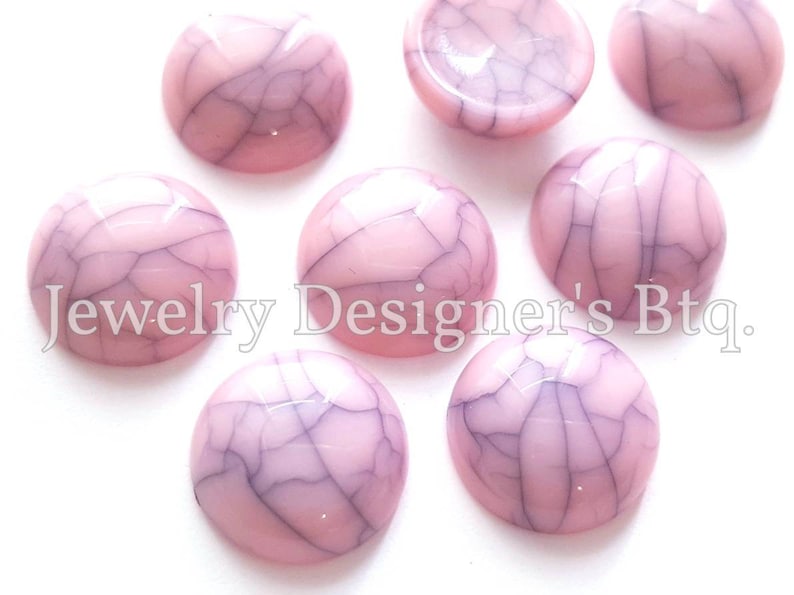 K&ouml;nnte beinhalten: Rosa und wei&szlig;e marmorierte Cabochons mit einer gecrackten Oberfl&auml;che. Die Cabochons sind rund und haben eine glatte, gl&auml;nzende Oberfl&auml;che.