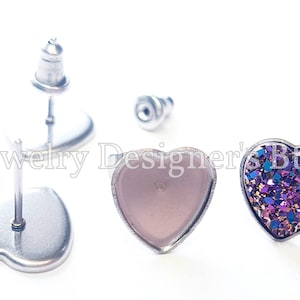 May include: A pair of heart-shaped earrings with silver posts. One earring has a clear, light pink heart-shaped cabochon, and the other earring has a heart-shaped cabochon with a purple, blue, and gold glitter design.