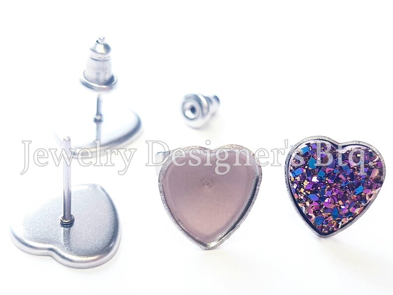 May include: A pair of heart-shaped earrings with silver posts. One earring has a clear, light pink heart-shaped cabochon, and the other earring has a heart-shaped cabochon with a purple, blue, and gold glitter design.