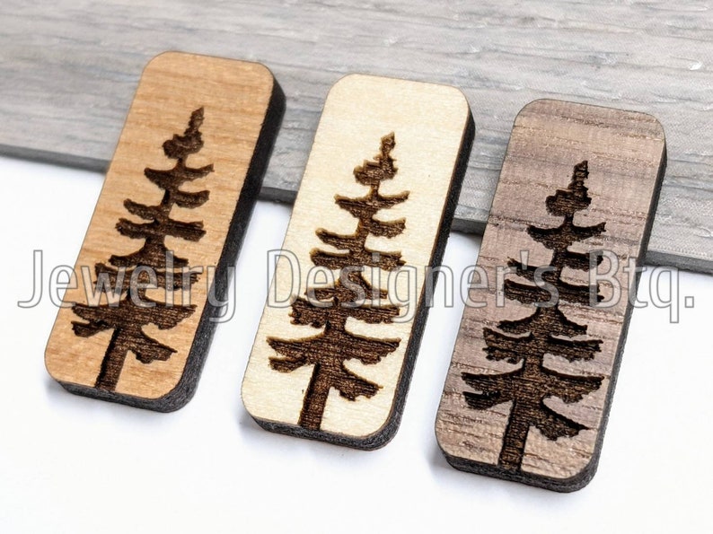 K&ouml;nnte beinhalten: Drei rechteckige Holzornamente mit einem lasergeschnittenen Design eines Kiefernbaums. Die Ornamente sind in drei verschiedenen Holzt&ouml;nen gehalten: hellbraun, natur und dunkelbraun.