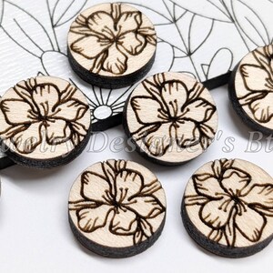 May include: Six round wooden embellishments with a laser-etched floral design. The embellishments are light brown with a dark brown outline.