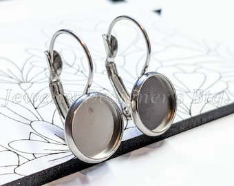 May include: A pair of silver earring blanks with round, flat, silver-toned metal settings. The settings are approximately 16mm in diameter.