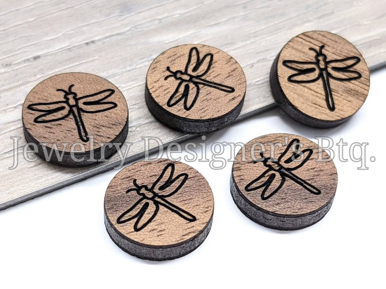 May include: Five round wooden discs with a black dragonfly design. The discs are approximately 1 inch in diameter.