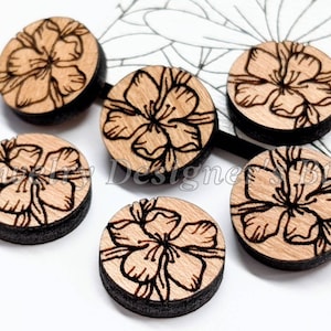 May include: Six round wooden embellishments with a laser-etched floral design. The embellishments are approximately 2.5 cm in diameter and have a natural wood colour.